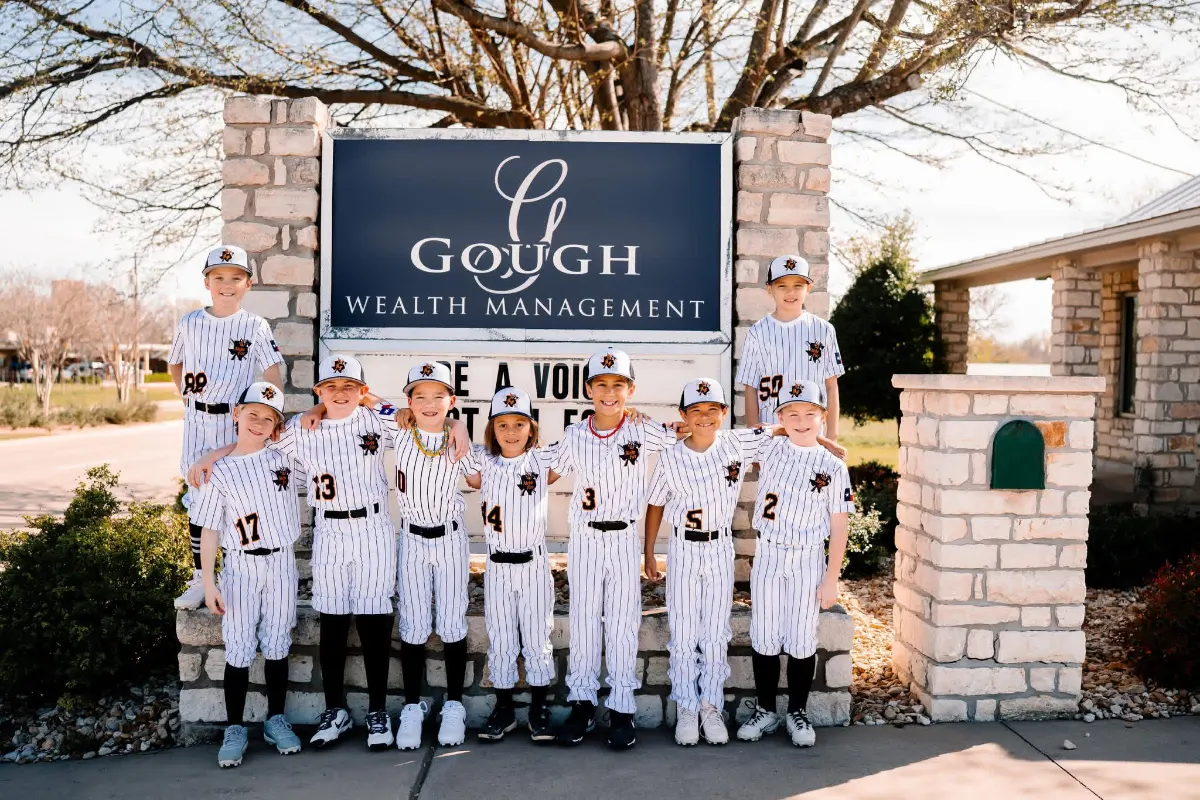 The Aledo Little League baseball team poses in front of a sign for one of their sponsors, Gough Wealth Management